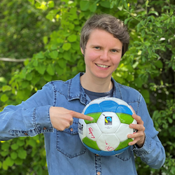Eine Frau zeigt auf einen Fußball, den sie in der linken Hand hält