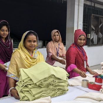 Vier bangladeschische Frauen stehen hinter einem Tisch voller Stoffe.