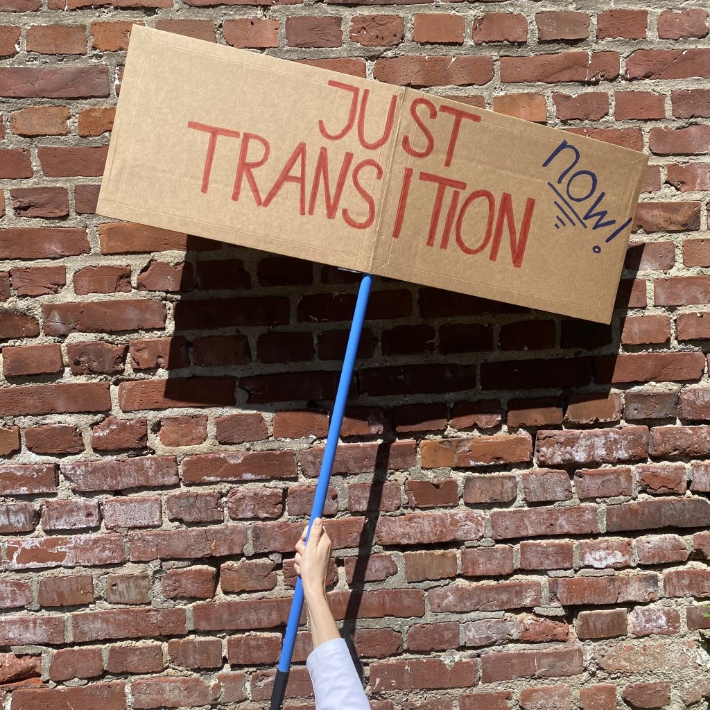 EIn Plakat mit Aufschrift "Just Transition" vor eine Backsteinwand.