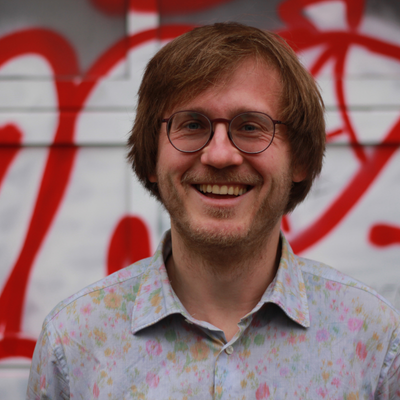 Ein Mann mit Brille steht vor einer Wand voller Graffiti