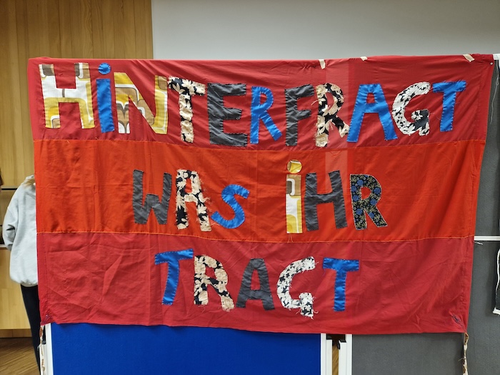 Ein Netzwerk, das Mut macht 8 Ein rotes Tuch, auf dem steht "Hinterfragt, was ihr tragt."