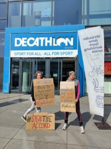 Wir brauchen verschärfte Sicherheitsabkommen 2 3 Personen stehen mit Schildern aus Pappe vor einem Decathlon-Geschäft.